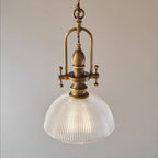 Close view of this Clérachic pendant's ribbed glass dome and brass cradle, lit, on a soft grey backdrop.