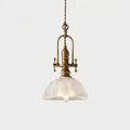 Clérachic pendant lit on a pale backdrop, with a brass cradle and a clear ribbed dome with a filament bulb inside.