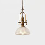 Clérachic pendant lit on a pale backdrop, with a brass cradle and a clear ribbed dome with a filament bulb inside.