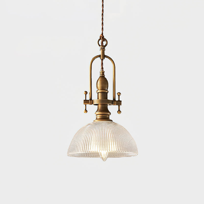 Clérachic pendant lit on a pale backdrop, with a brass cradle and a clear ribbed dome with a filament bulb inside.