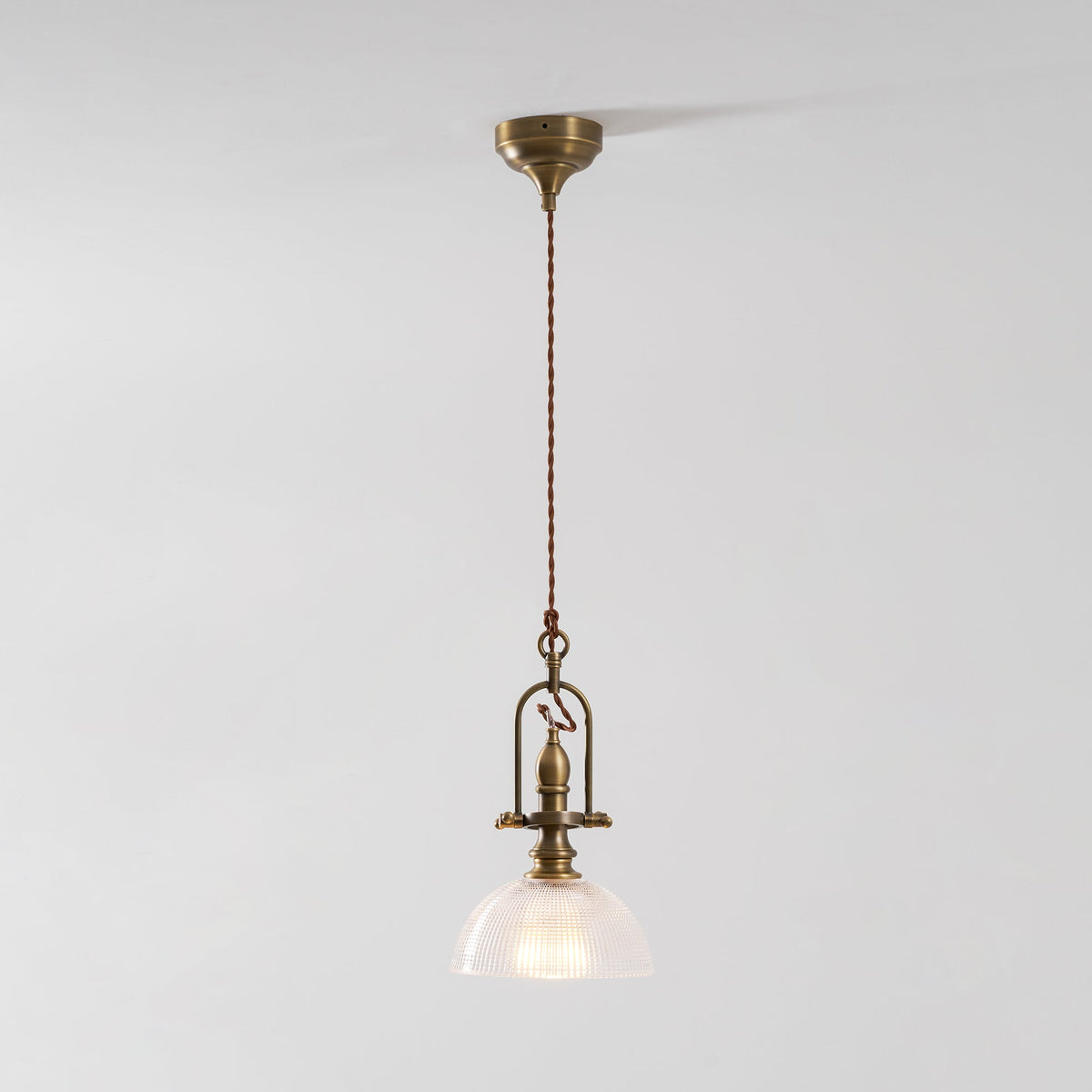 A Clérachic pendant on a light grey backdrop, with its brass canopy, a long cord and a ribbed glass dome.