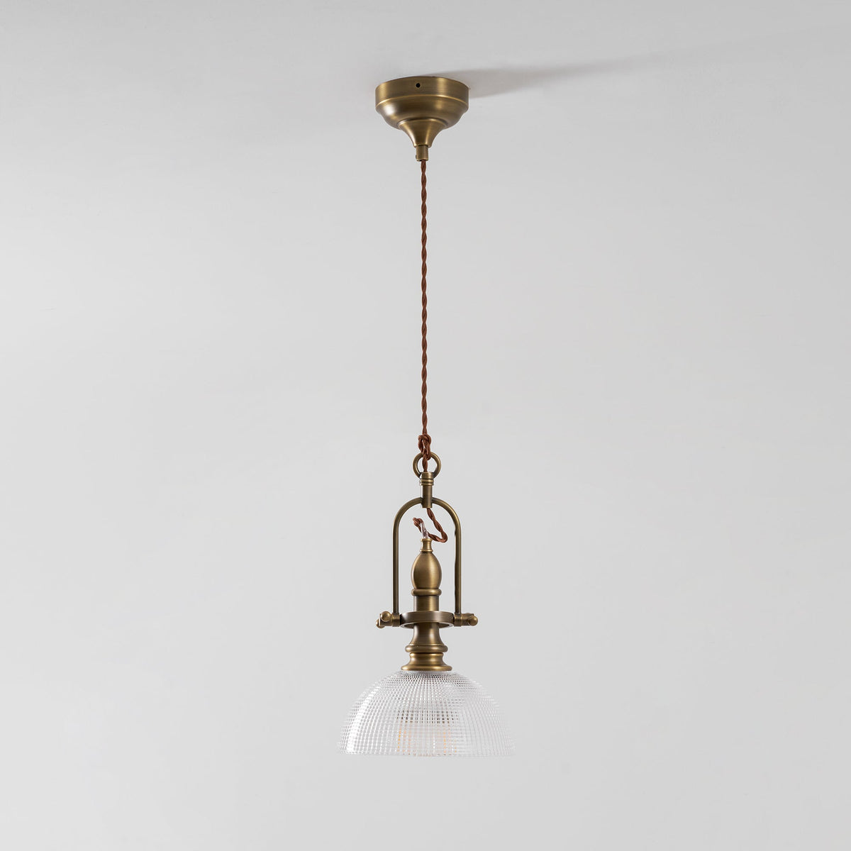 Clérachic pendant from a distance on a pale wall, with a brass canopy, a twisted cord and a small glass dome.