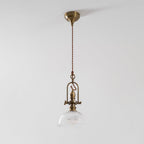 A Clérachic pendant with a brass canopy and long twisted cord, with the glass dome lit softly against a pale ceiling.