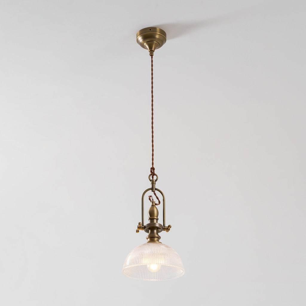 Clérachic pendant lit against a pale grey wall, with a brass canopy, a twisted cord and a ribbed glass dome.