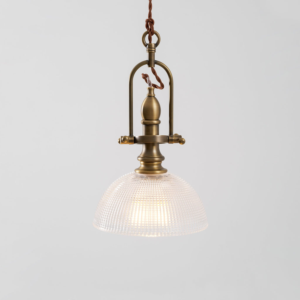 Close view of the brass cradle and clear ribbed dome on this Clérachic pendant, with a warm bulb inside.