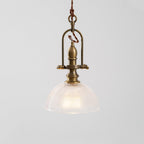 Close view of the brass cradle and clear ribbed dome on this Clérachic pendant, with a warm bulb inside.