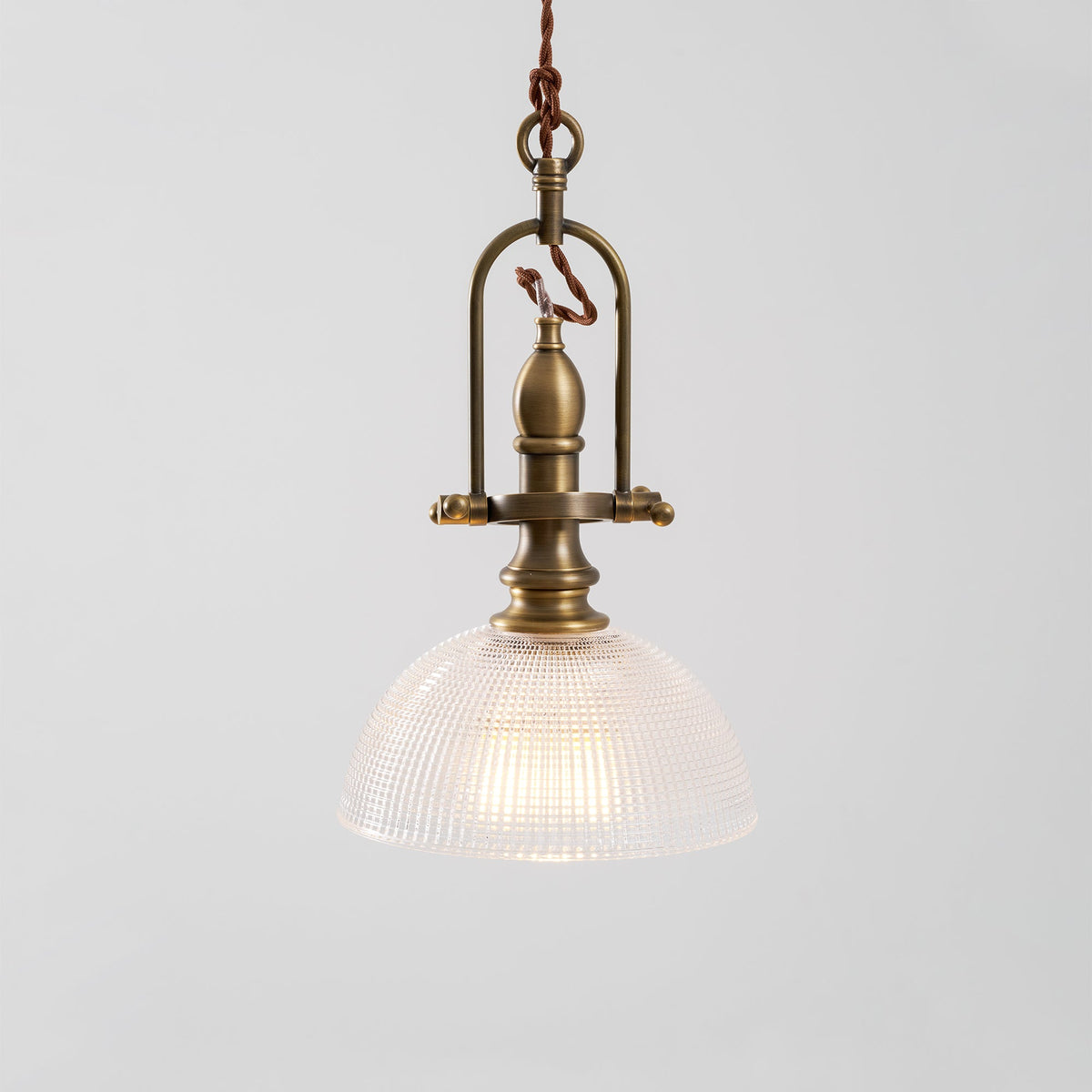 Close view of the brass cradle and clear ribbed dome on this Clérachic pendant, with a warm bulb inside.