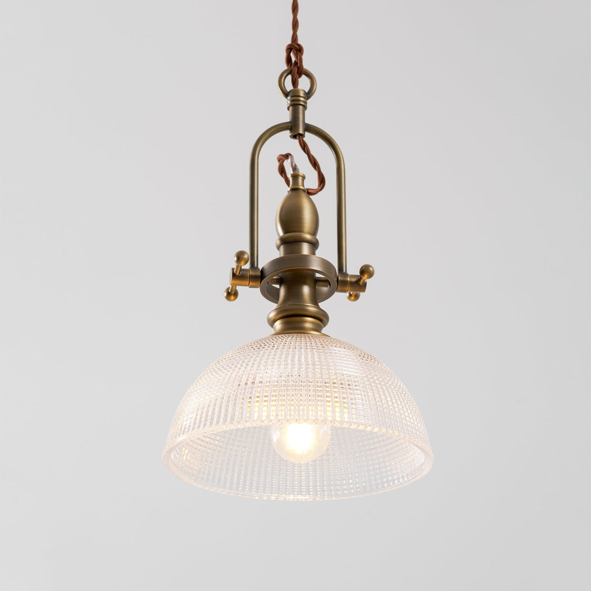 Clérachic pendant seen from the front, with an open brass cradle and a clear dome, and a filament bulb at its centre.