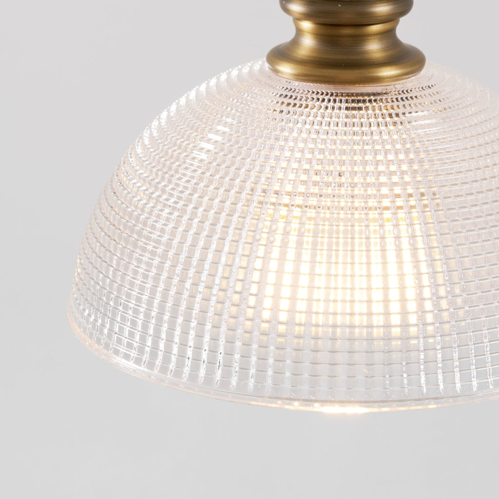 Close view of the lit glass dome and brass collar on this Clérachic pendant, with a warm glow through the grid pattern.