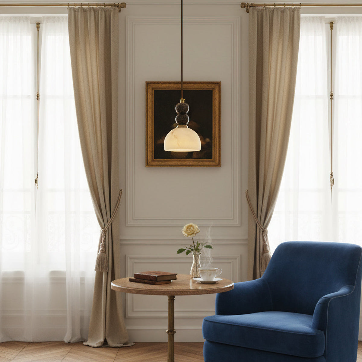 Clérachic pendant light hung low beside a framed painting, with a blue velvet armchair and small round table below.