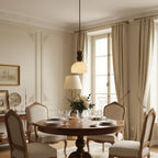 Clérachic pendant light above a round wooden dining table laid for a meal, in a classic room with tall windows and curtains.
