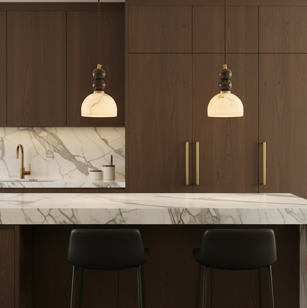 Two Clérachic pendant lights lit above a marble-topped kitchen island, in front of dark walnut cabinets with gold handles.