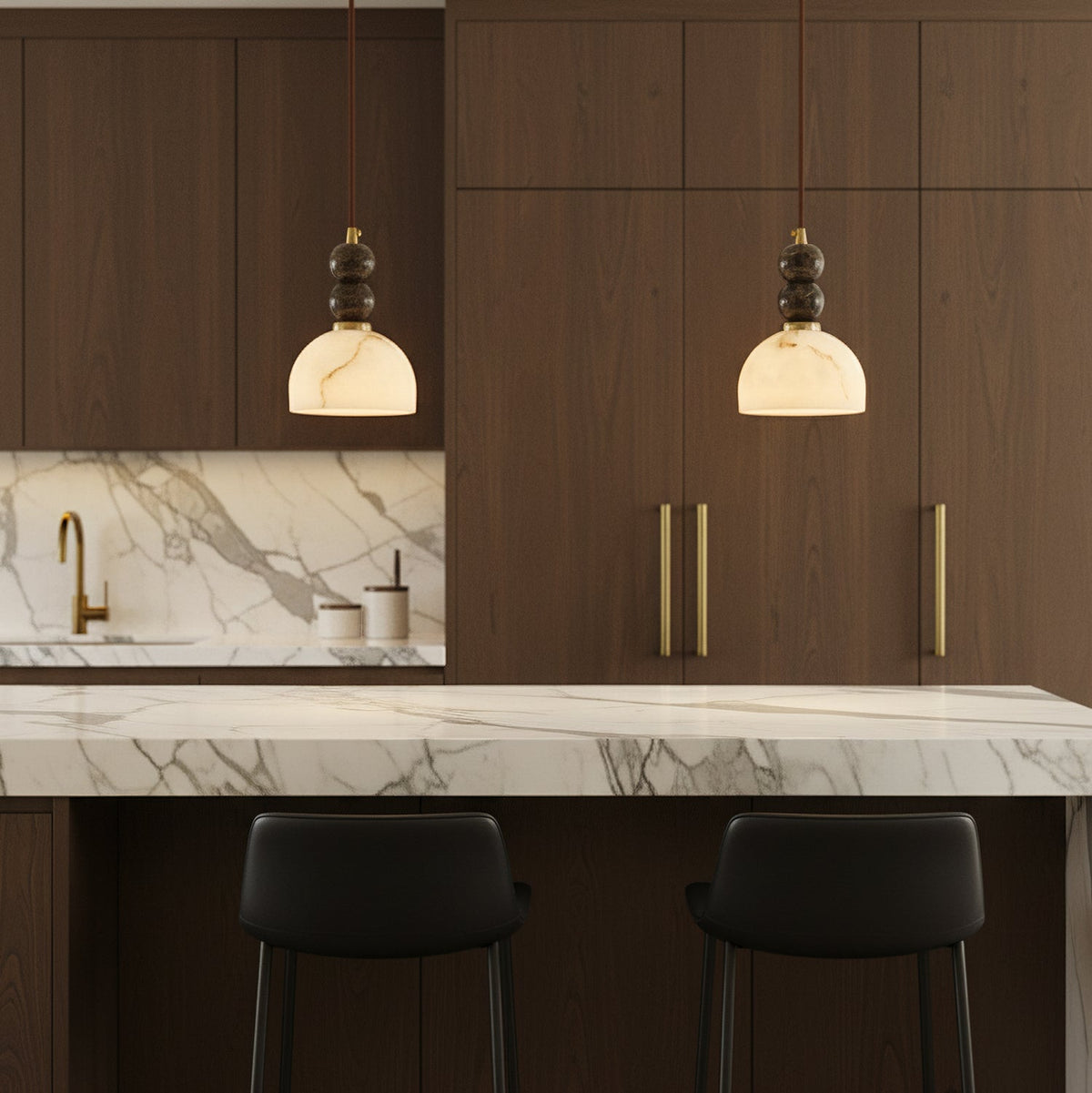 Two Clérachic pendant lights lit above a marble-topped kitchen island, in front of dark walnut cabinets with gold handles.