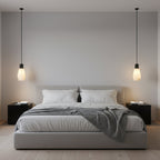 A pair of narrow Clérachic pendant lights hang beside a grey bed as bedside lamps, each glowing warm.