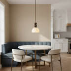 This Clérachic pendant light hangs over a round marble table with white chairs, in front of a blue banquette in a kitchen.