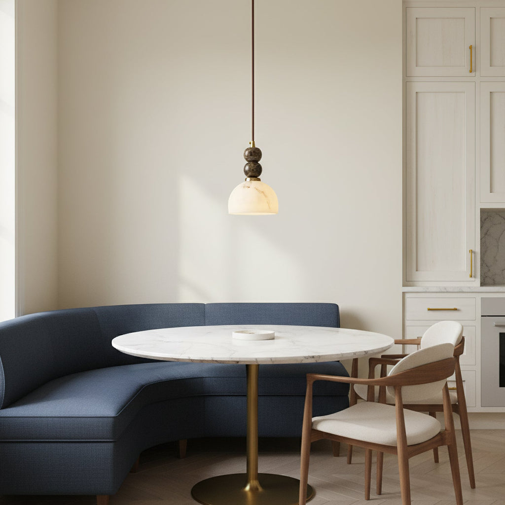 A Clérachic pendant light above a round white table, with a curved blue sofa and wooden chairs in a pale kitchen nook.