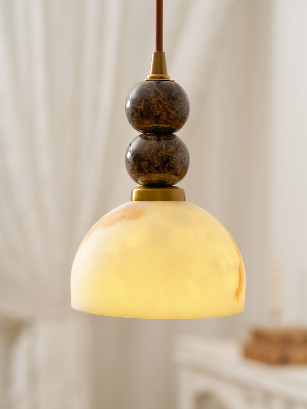 Close view of the dome-shaped faux alabaster shade and two dark marble spheres on this Clérachic pendant light, with sheer curtains blurred behind.