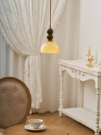This Clérachic pendant light lit warm in front of a lace curtain, with a teacup on a table and a white console behind.