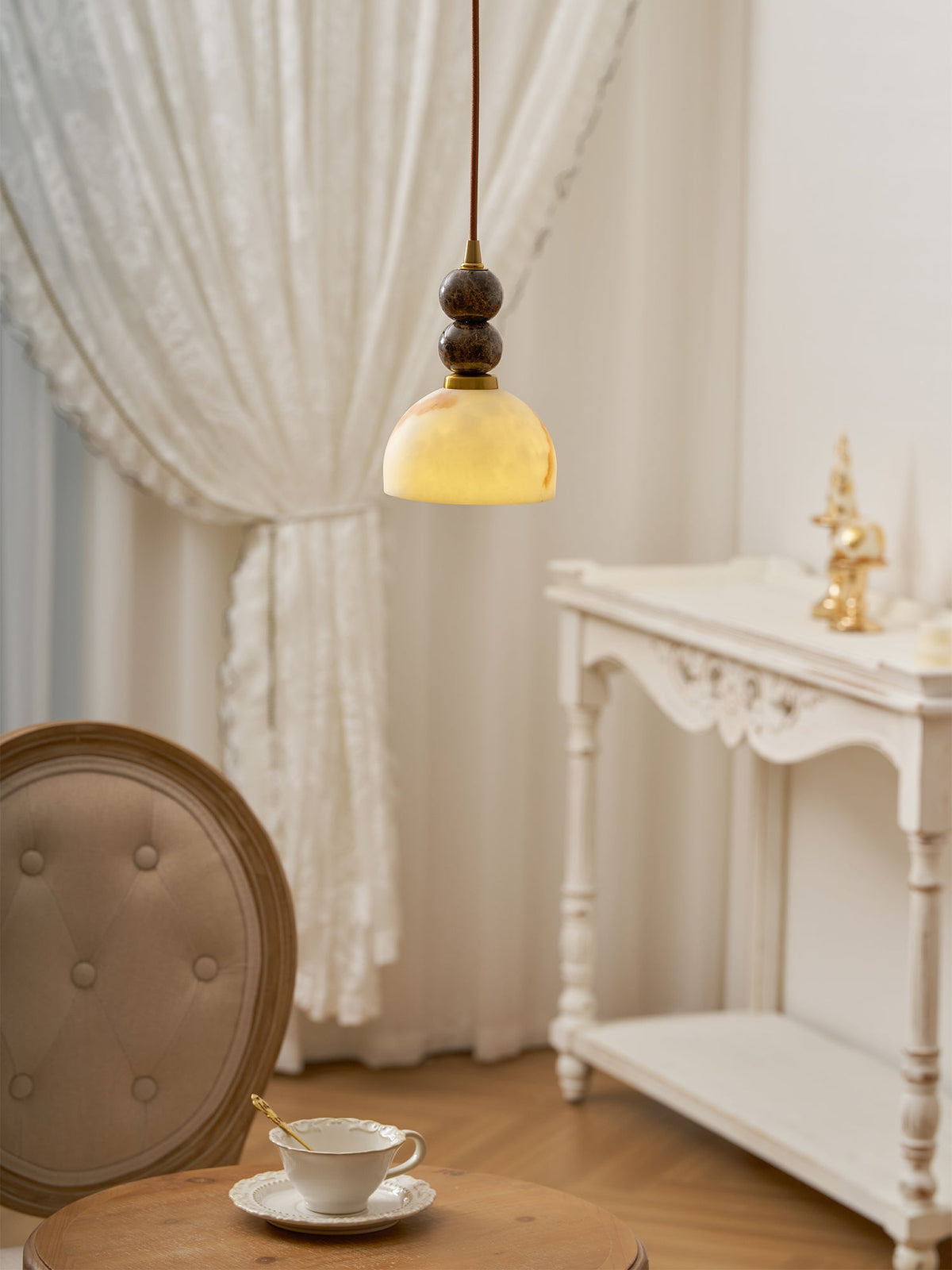 This Clérachic pendant light lit warm in front of a lace curtain, with a teacup on a table and a white console behind.