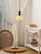 A Clérachic pendant light glowing yellow above a small round table with a teacup, beside a white carved console.