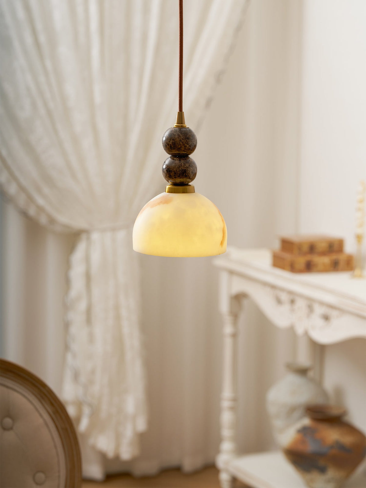 Close view of a lit Clérachic pendant light, its marble spheres and brass cap above a softly glowing dome shade.