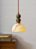 Clérachic pendant light with a veined dome shade, hanging beside a wooden cabinet with books on a plain grey wall.