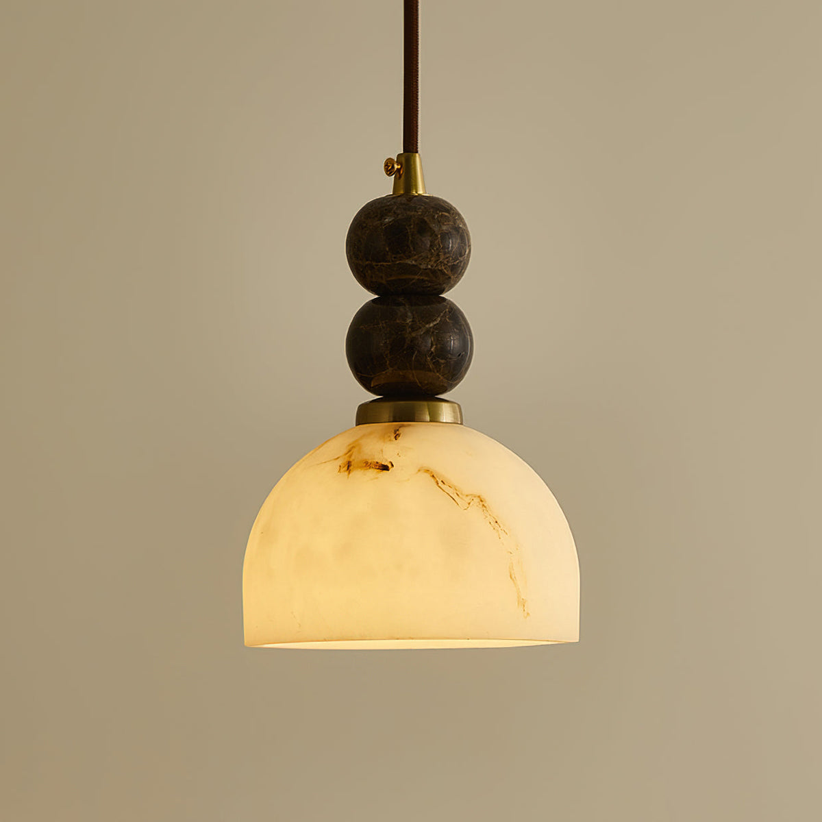 Close view of the two dark marble spheres and brass collar above the veined dome shade of this Clérachic pendant light.