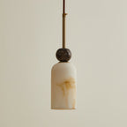 This Clérachic pendant light has a slim, rounded cylinder shade under a dark marble ball and a brass rod, on a warm cream backdrop.