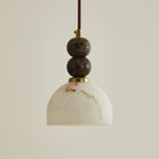 Unlit dome shade of faux alabaster hanging below two stacked dark marble spheres on this Clérachic pendant light.