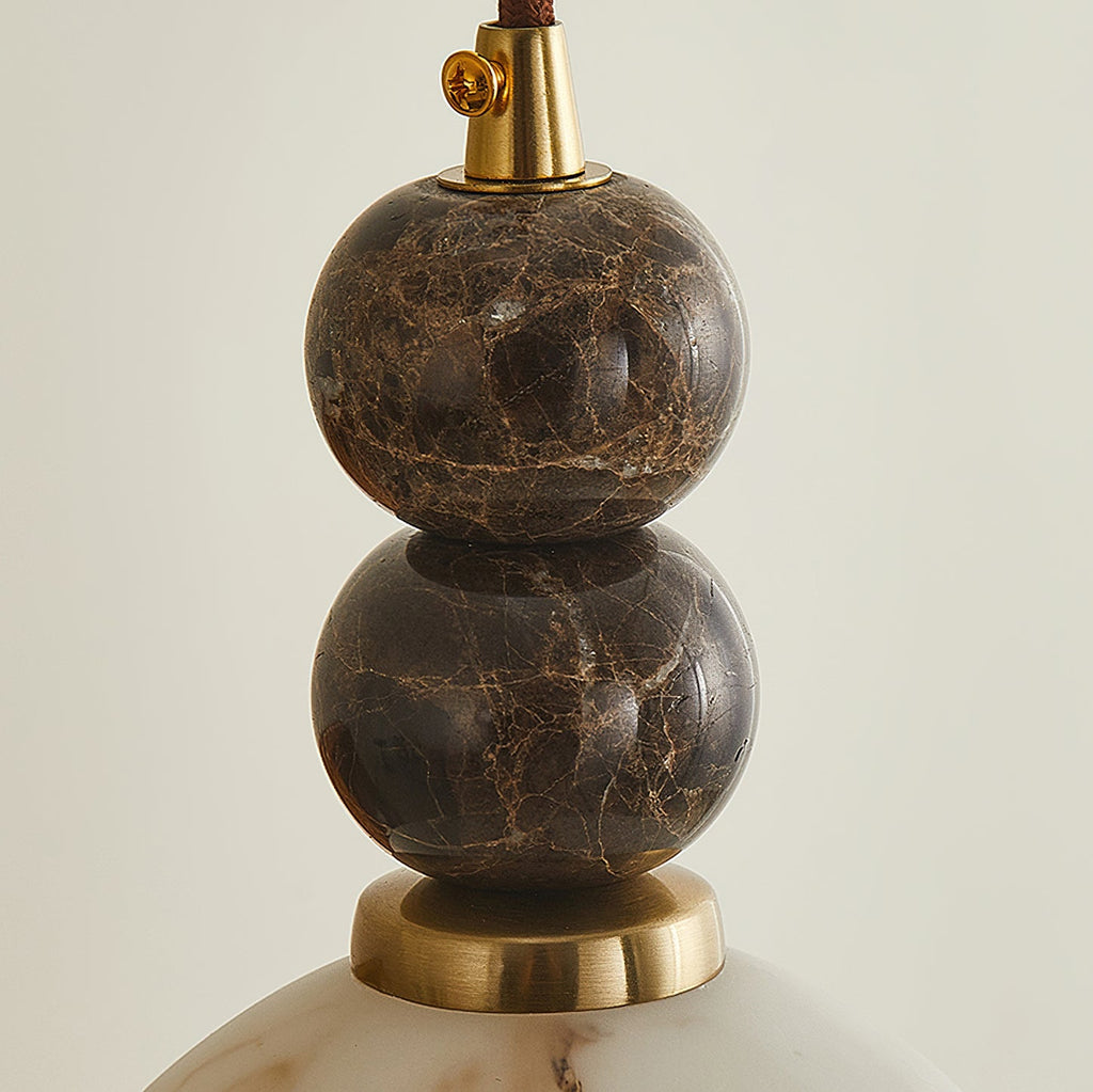 Close view of two stacked dark marble spheres with brown veining, above a brass ring, on this Clérachic pendant light.