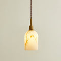 Lit Clérachic pendant light with a rounded cylinder shade, glowing warm with brown veining and a brass cap on a twisted cord.