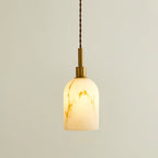 Lit Clérachic pendant light with a rounded cylinder shade, glowing warm with brown veining and a brass cap on a twisted cord.