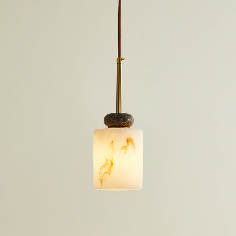 Lit short cylinder shade on this Clérachic pendant light, with a dark marble disc, brass rod and brown cord above.