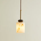 Lit short cylinder shade on this Clérachic pendant light, with a dark marble disc, brass rod and brown cord above.