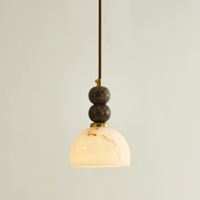Lit Clérachic pendant light with a dome shade glowing white and two dark marble spheres on a brown cord.