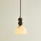 Lit Clérachic pendant light with a dome shade glowing white and two dark marble spheres on a brown cord.