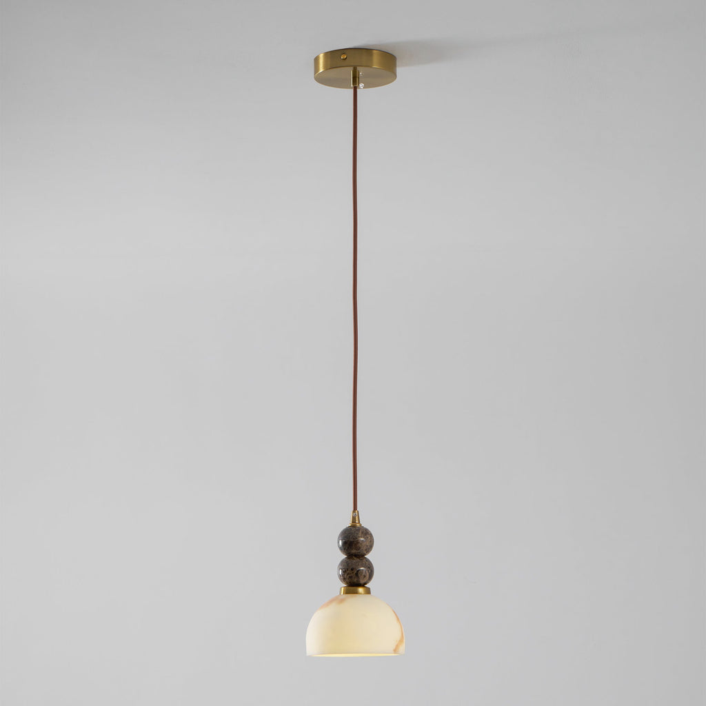 Full length of this Clérachic pendant light, lit, hanging on a thin brown cord from a brass ceiling plate against a grey wall.