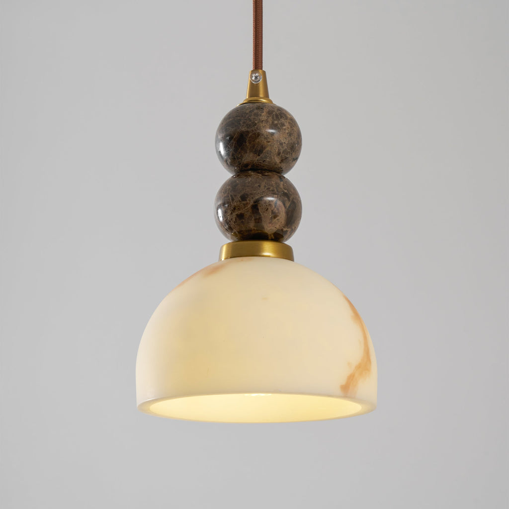 Lit dome shade of this Clérachic pendant light glowing creamy yellow, below two dark marble spheres on a brown cord.