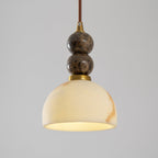 Lit dome shade of this Clérachic pendant light glowing creamy yellow, below two dark marble spheres on a brown cord.