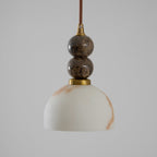 Unlit Clérachic pendant light with a dome shade and two dark marble spheres on a brown cord, against a plain grey backdrop.