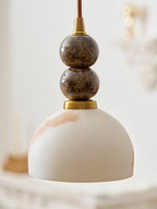 This Clérachic pendant light has a pale dome shade veined with peach, hung in front of an ornate white console and a mirror.