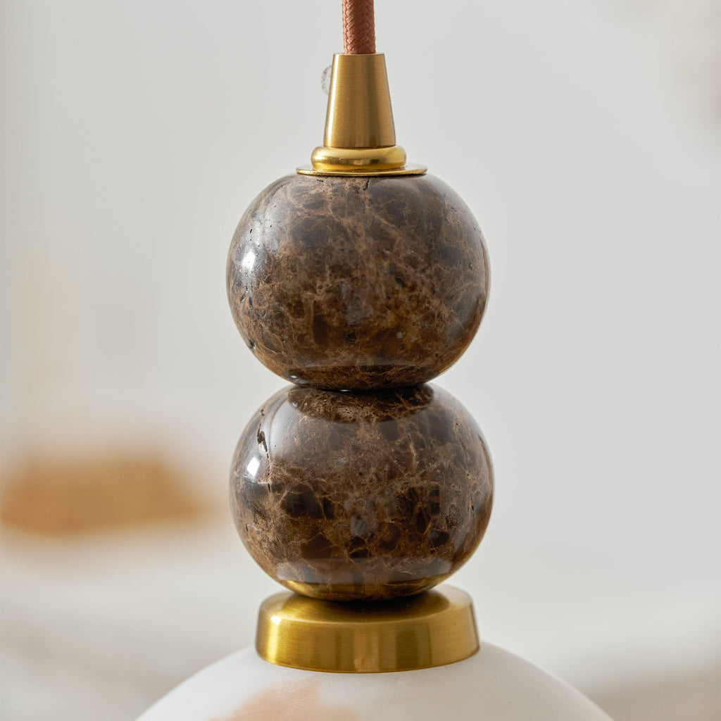 Close view of the brown-veined marble spheres and brass fittings above the shade of this Clérachic pendant light.