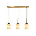 Three short cylinder shades with dark marble discs hang from the brass bar of this Clérachic pendant light.