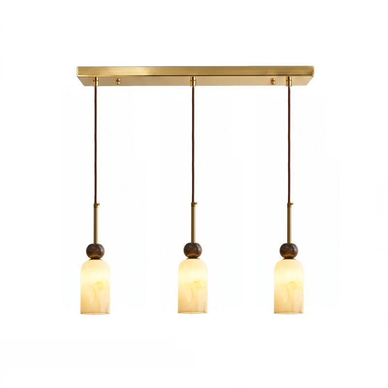 Three narrow rounded cylinder shades glow warm below the brass rectangular canopy of this Clérachic 3-light pendant.