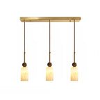 Three narrow rounded cylinder shades glow warm below the brass rectangular canopy of this Clérachic 3-light pendant.