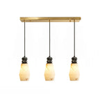 Three tapered, faceted shades with black cords hang from the brass bar of this Clérachic 3-light pendant light.