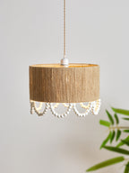 Beside a leafy plant, this Clérachic pendant hangs lit on its twisted cord from a round ceiling canopy.