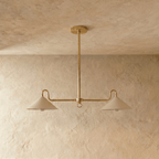 A polished brass Clérachic pendant light shown from below, both cone shades lit above a plaster wall.