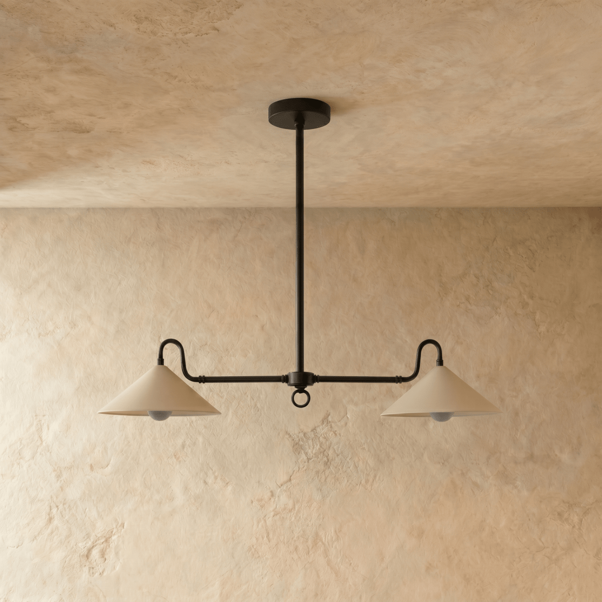 A black Clérachic pendant light viewed from below, its two cone shades lit against a plaster wall.