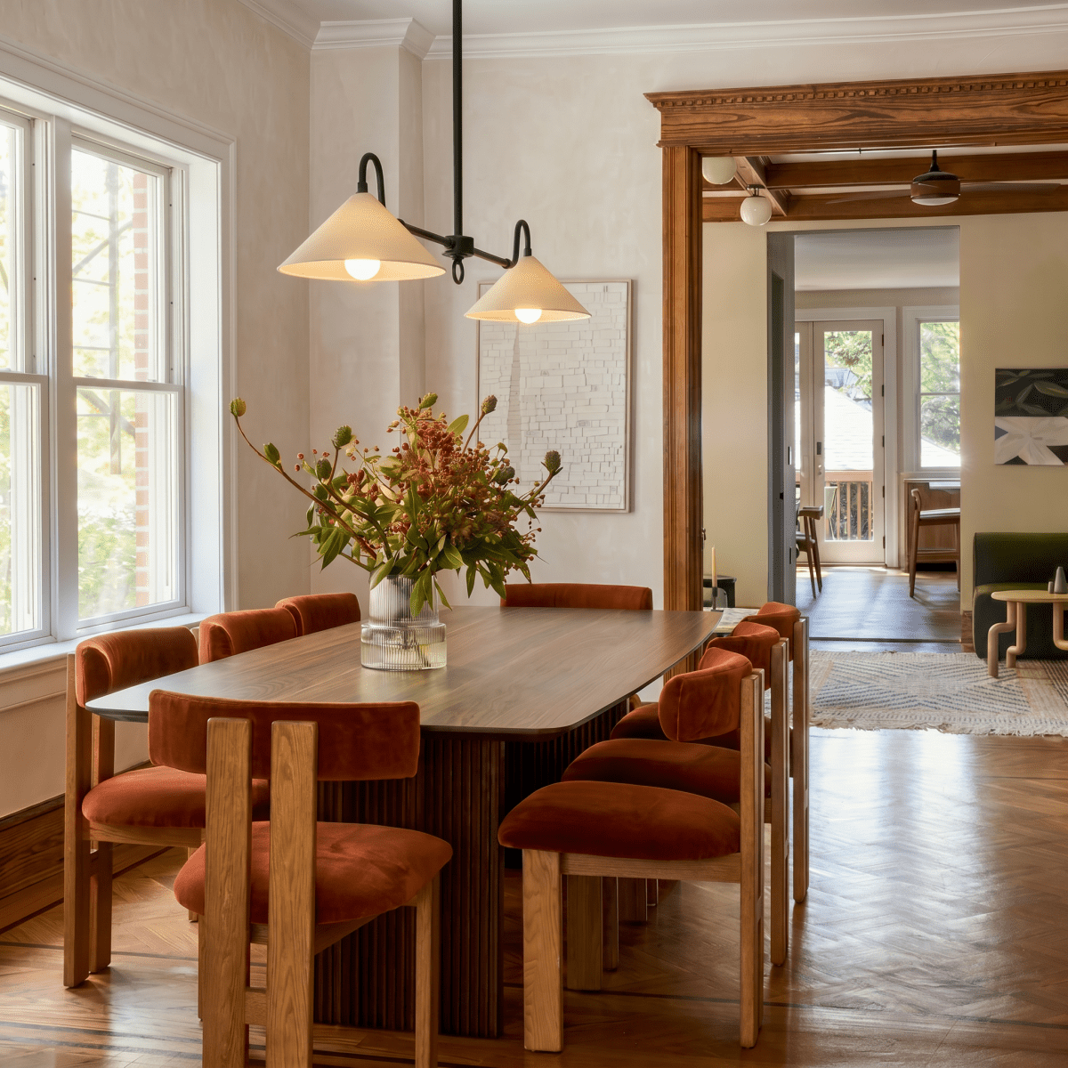 This black Clérachic pendant light hangs over a walnut dining table set with rust velvet chairs.
